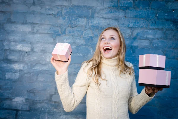 Attraente bionda giovane donna in maglione di lana che riceve regali divertirsi felice sorridente su sfondo muro di mattoni blu — Foto Stock