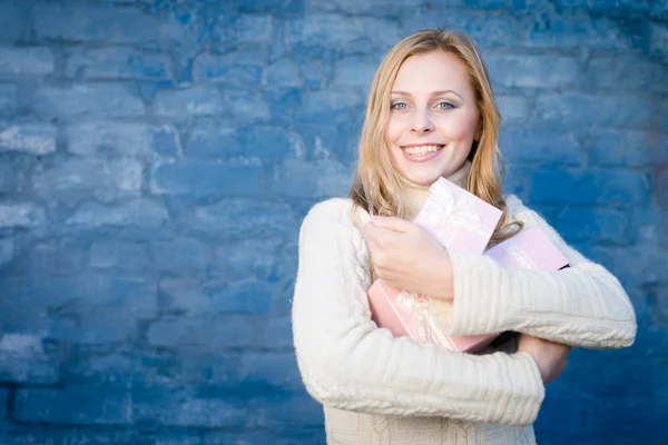 Atractiva mujer joven rubia en suéter de lana recibiendo regalos divertirse feliz sonriendo sobre fondo de pared de ladrillo azul —  Fotos de Stock