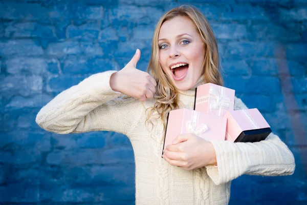 Attraktiv blond ung kvinna i ylle tröja får presenter har roligt glada leende på blå tegel vägg bakgrund — Stockfoto