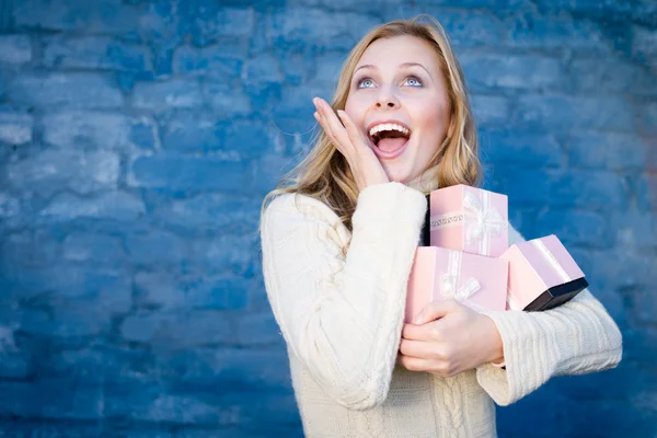 Atractiva mujer joven rubia en suéter de lana recibiendo regalos divertirse feliz sonriendo sobre fondo de pared de ladrillo azul —  Fotos de Stock