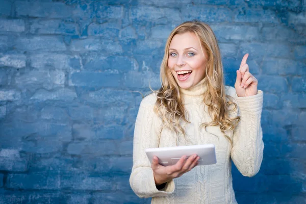 Image of beautiful blond young lady in white wool sweater using tablet pc at blue concrete wall copy space background — Stock Photo, Image