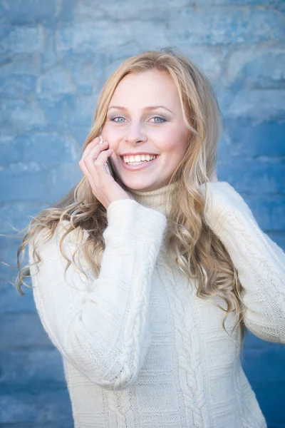 Image de belle jeune femme blonde en chandail de laine blanche parlant sur mobile à fond bleu mur de béton copie espace — Photo