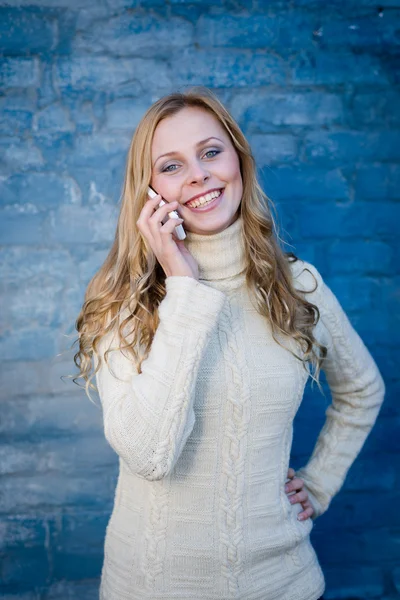 Bild der schönen blonden jungen Dame in weißem Wollpullover spricht auf Handy an blauer Betonwand Kopierraum Hintergrund — Stockfoto