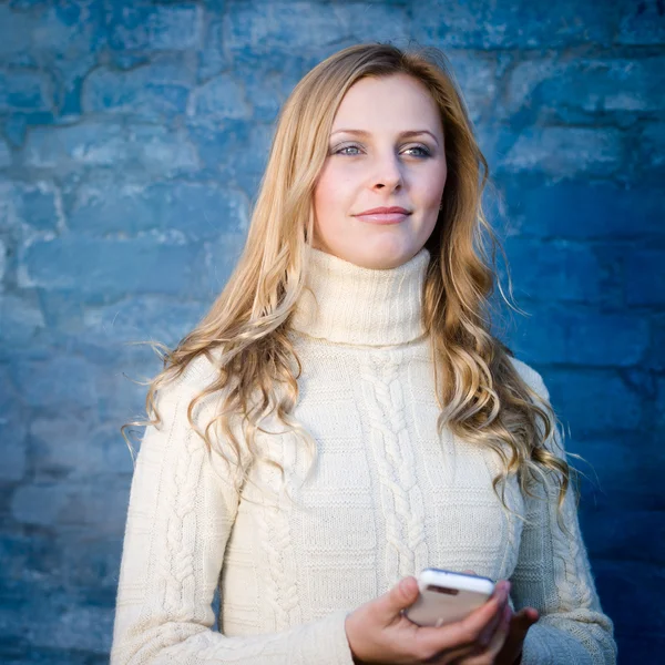 Imagem da bela loira jovem senhora em camisola de lã branca mensagem de texto móvel na parede de concreto azul cópia espaço fundo — Fotografia de Stock
