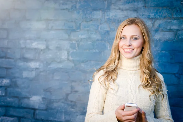 コピー領域の背景の水色のコンクリート壁で白いウール セーター テキスト メッセージ携帯メッセージで美しい金髪の若い女性の画像 — ストック写真
