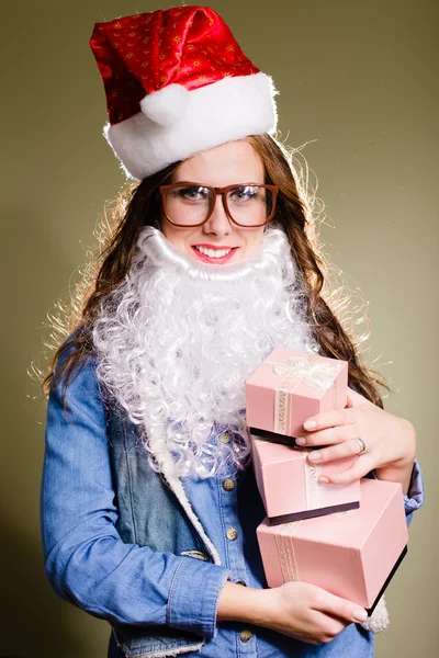 Funny hipster girl in super size eyeglasses wearing xmas santa hat and faux beard holding three boxes of presents over olive copy space background — Stock Photo, Image