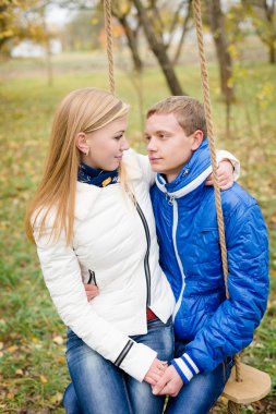 Mutlu genç çift açık havada soğuk sonbahar gün salıncağa oturan üzerinde