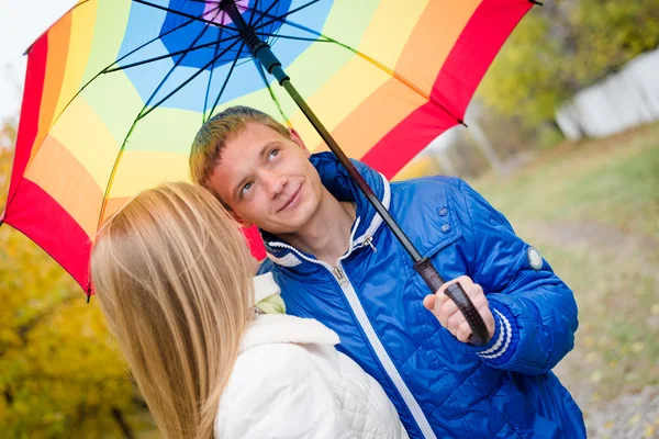 Ευτυχισμένο ζευγάρι εφήβων που περπάτημα σε εξωτερικούς χώρους σε κρύα ημέρα του φθινοπώρου κάτω από ομπρέλα φωτεινό — Φωτογραφία Αρχείου