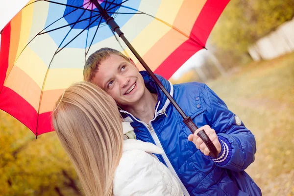 Happy teen couple walking outdoors on cold autumn day under bright umbrella — Stock Photo, Image