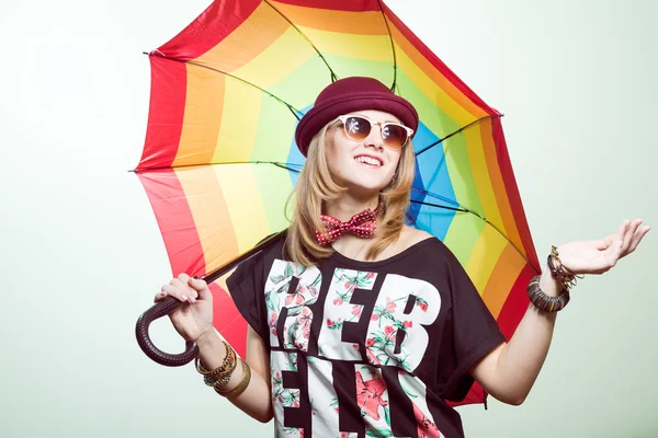 Studio portrait of teenage hipster girl wearing trendy hat and sunglasses with colorful umbrella over olive copy space background — Stock Photo, Image