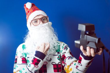 Noel Baba sakal selfie retro kamera üzerinde mavi arka plan stüdyo portre ile yapım komik genç hipster adam