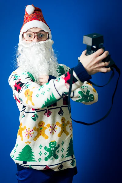 Funny young hipster man in santa beard making selfie with retro camera on blue background studio portrait — Stock Photo, Image