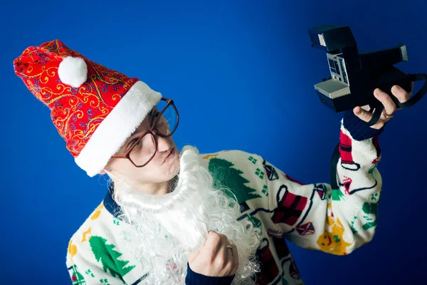 Funny young hipster man in santa beard making selfie with retro camera on blue background studio portrait — Stock Photo, Image