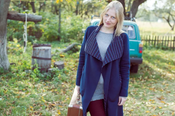 Jeune femme en manteau rétro avec valise vintage en attente dans le parc d'automne fond copyspace — Photo