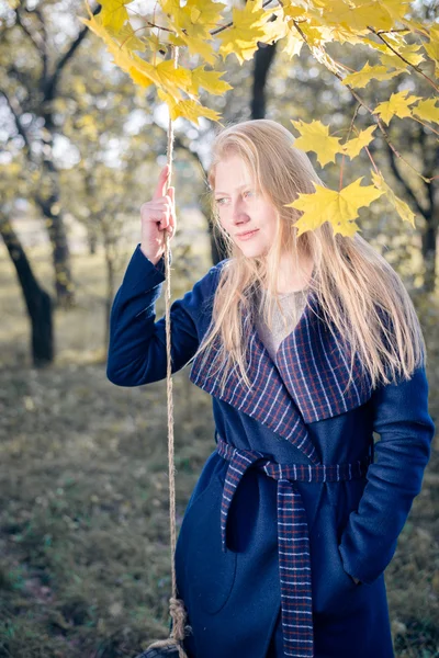 Retrato de elegante hermosa rubia joven divirtiéndose en la cuerda swing feliz sonriendo y mirando a la cámara en el espacio de copia de otoño al aire libre fondo —  Fotos de Stock