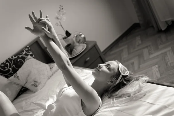 Женщина с повязкой для сна лежит на кровати — стоковое фото