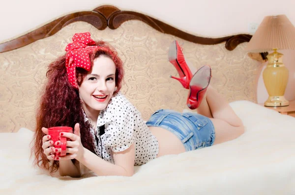 Sexy girl in bed holding red cup of hot drink — Zdjęcie stockowe