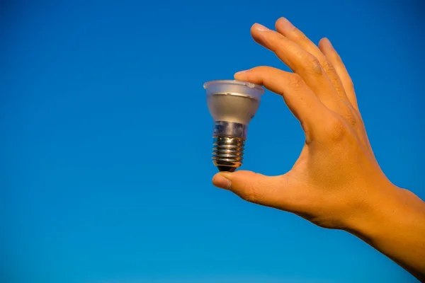 La mano sostiene la lámpara led contra el cielo azul — Foto de Stock