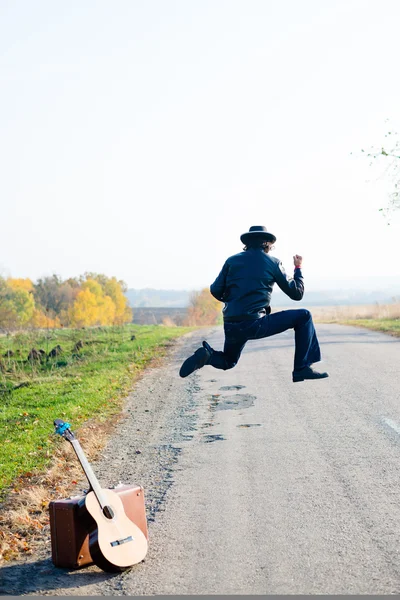 Man with suitcase and guitar jumping crazy — Stock Photo, Image