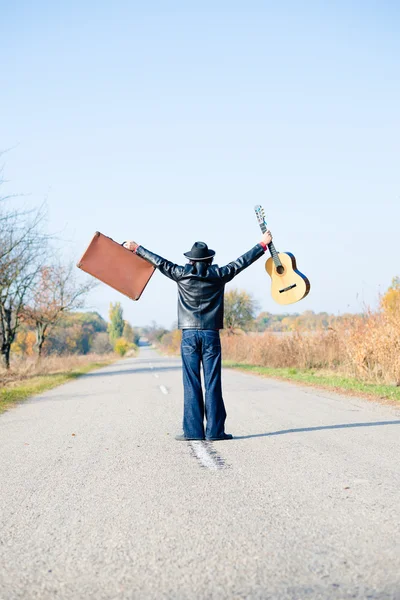 Man holding hands up with suitcase and guitar — Stockfoto