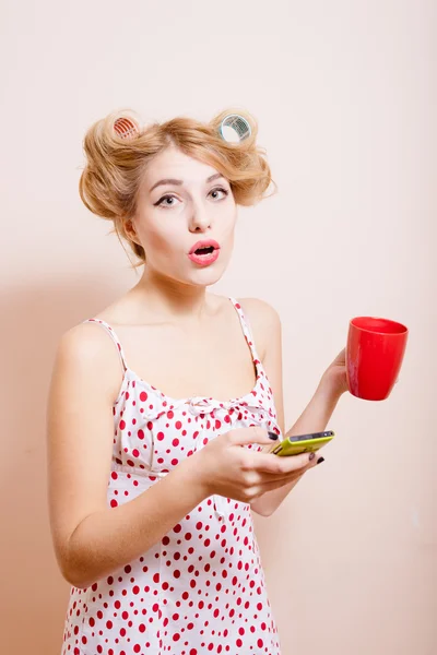 Пинап леди в бигуди с чашкой и мобильным — стоковое фото