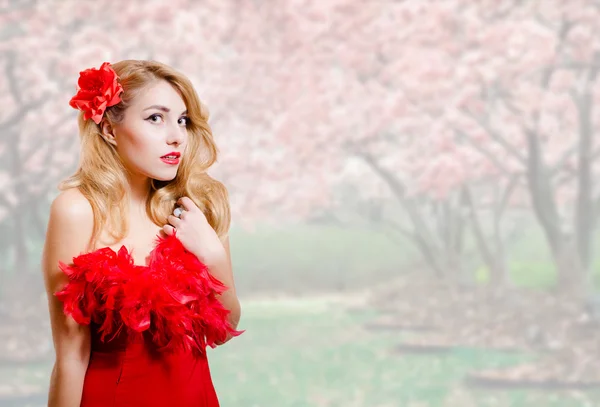 Beautiful young woman in red dress on garden blossom background — Stock Photo, Image