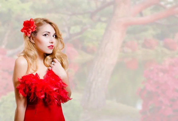 정원 꽃 배경에 빨간 드레스에 아름 다운 젊은 여자 — 스톡 사진