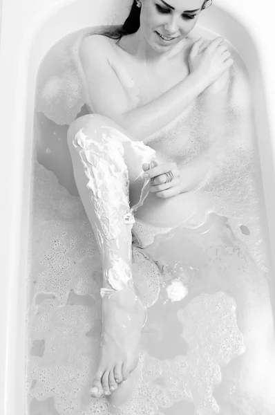 Jolie femme rasage jambe dans le bain de mousse sourire heureux — Photo