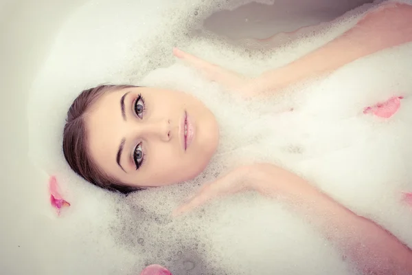 Hermosa mujer acostada en baño de espuma de burbuja con pétalos de rosa —  Fotos de Stock