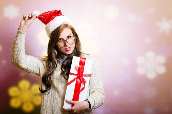 Pretty woman in Santa hat holding giftbox on fastive background. — Zdjęcie stockowe