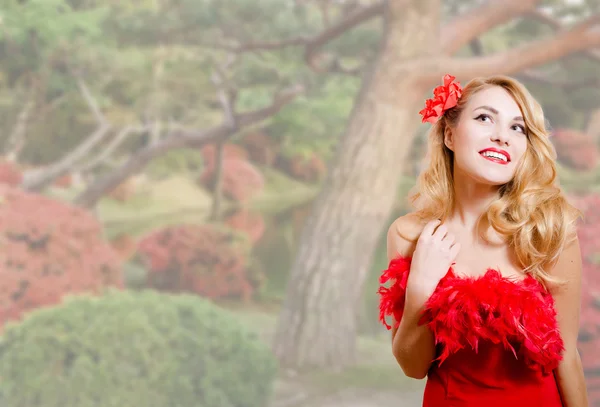 Krásná mladá žena v červených šatech na zahradní květy pozadí — Stock fotografie