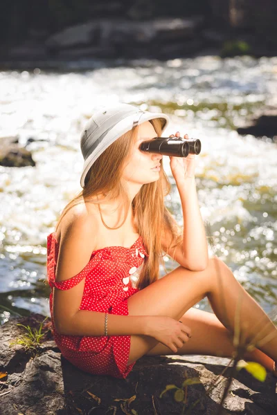 Young sexy female in red dress and pithhelmet using binoculars — Stok fotoğraf