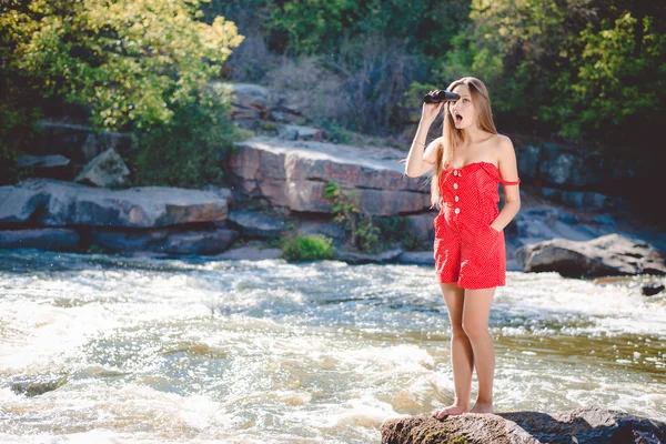 Young surprised female using binoculars on the riverbank — Stok fotoğraf