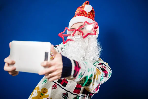 Weihnachtsmann auf blauem Hintergrund macht Selfie mit Tablet-PC — Stockfoto