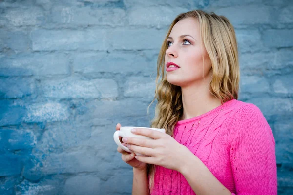 Attraktiv ung kvinna håller cup av dryck mot tegelvägg. — Stockfoto