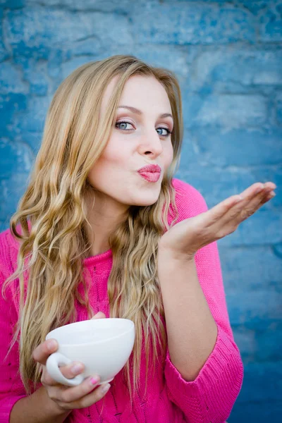 Happy smiling girl holding cup of beverage against brick wall. — Stock Photo, Image