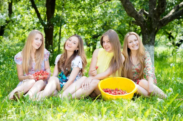 Чотири молодих друзів весело їдять полуницю з величезної миски — стокове фото