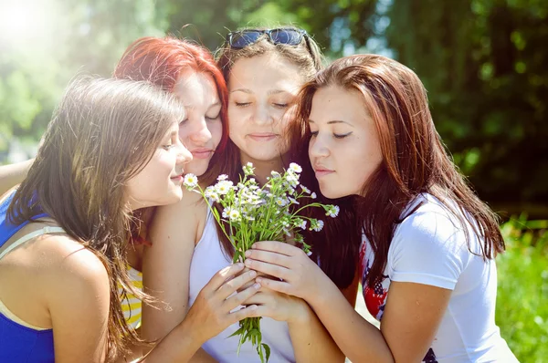 Quatro amigos bonitos felizes que jogam com flores na grama verde — Fotografia de Stock