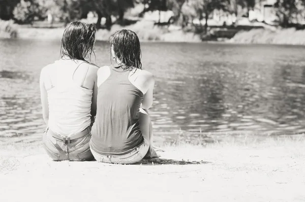 Twee vrouwelijke zittend terug naar camera op zomer strand buitenshuis — Stockfoto