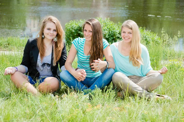 Tres relajantes hermosas mujeres coqueteando se sientan en la hierba verde —  Fotos de Stock