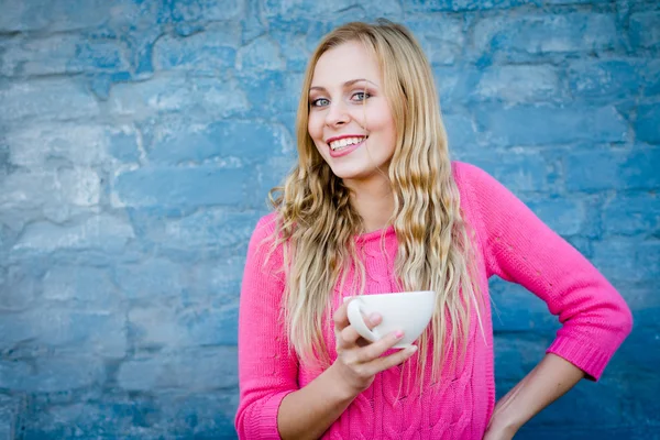 Feliz chica sonriente sosteniendo la taza de bebida sobre la pared de ladrillo . — Foto de Stock