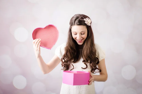 Beautiful young lady looking at heart box on bokeh background — Stock Photo, Image
