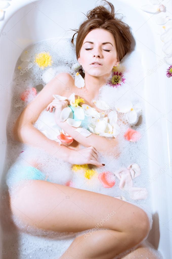 Beautiful sexy young woman having bath with flower petals