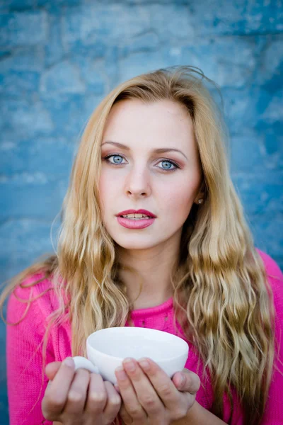 Feliz chica sonriente sosteniendo taza de bebida sobre fondo azul — Foto de Stock