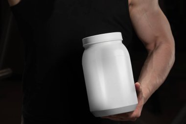 Spor tozu için kapağı olan beyaz parlak plastik kavanoz. Protein, vitamin, bcaa, sporcunun elinde tabletler.