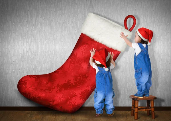 Funny Little twins dressed Santa hat, hangs big Christmas stocki — Stock Photo, Image