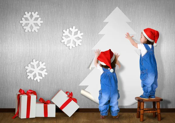 Funny Little twins dressed Santa hat, glue Christmas tree on wal — Stock Photo, Image