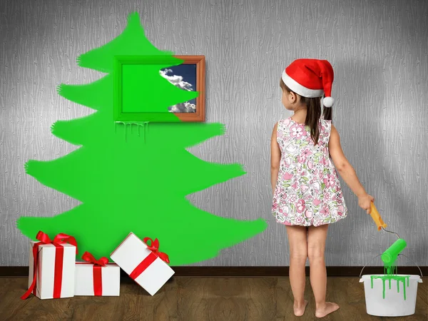 Funny enfant fille habillé chapeau de Père Noël, dessine arbre de Noël sur le mur — Photo