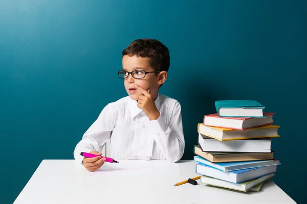 Niño lindo pensativo con gafas sentadas en una mesa — Foto de Stock