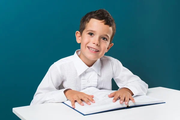 Rapaz sorridente com livro na mesa — Fotografia de Stock